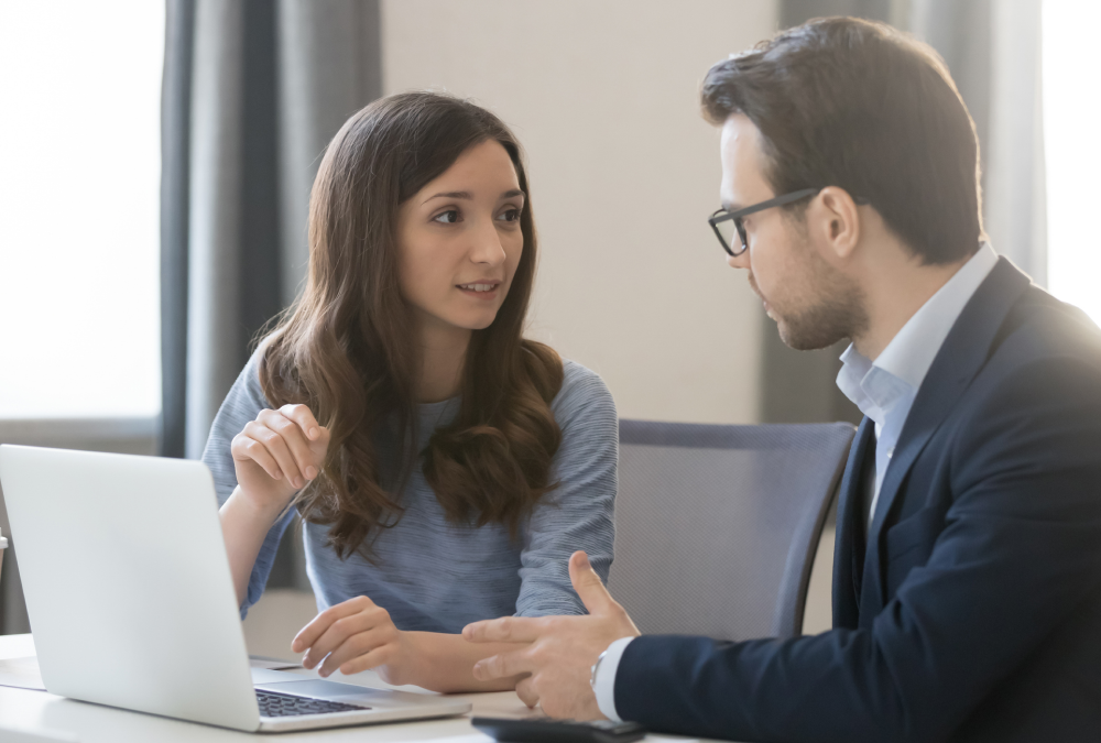 Two colleagues discussing work at desk.