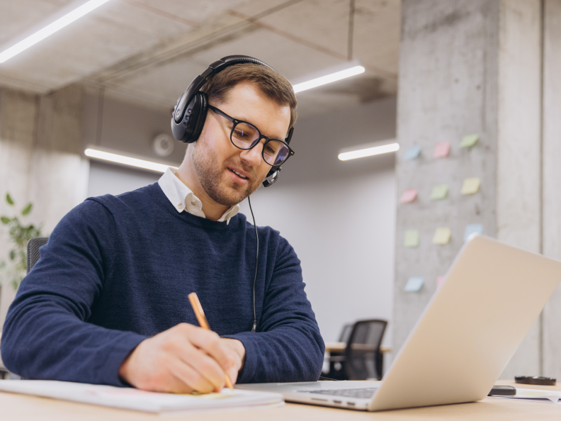 Man writing notes while wearing headphones.