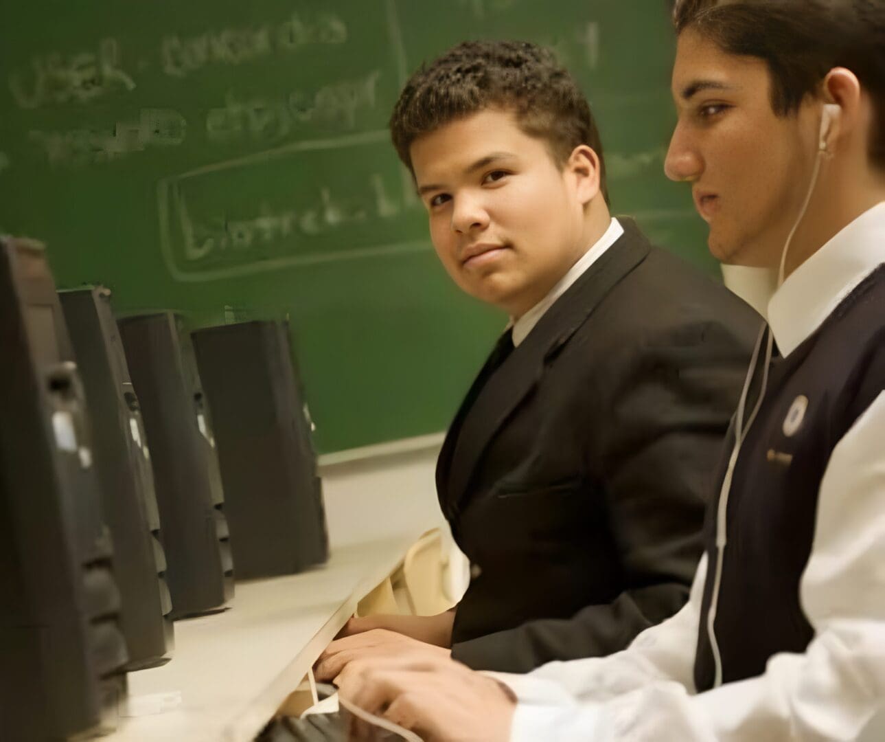 Two students in formal uniforms sitting in a computer lab.